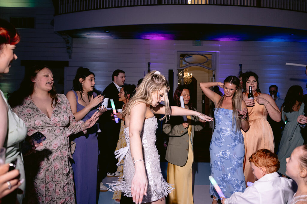 High-energy wedding reception dance floor featuring the bride, groom, family, and guests celebrating with lively dancing, glow sticks, bouquet toss moments, and joyful party atmosphere at The French Farmhouse wedding venue in Collinsville, Texas.